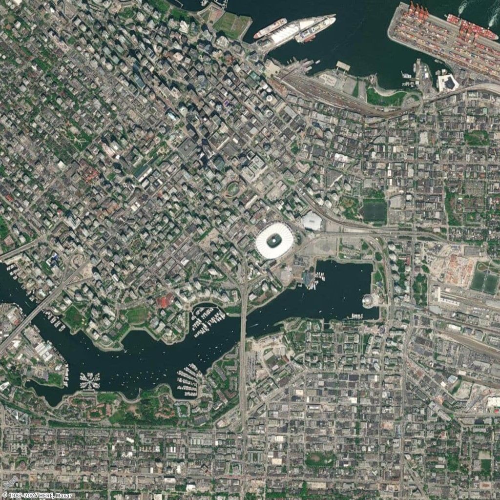 Aerial view of a coastal city with dense urban layout, harbor, and large stadium visible.