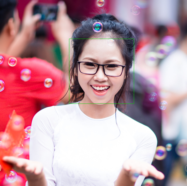 眼鏡をかけ、微笑んでいる若い女性。周りにシャボン玉が浮かんでいる。