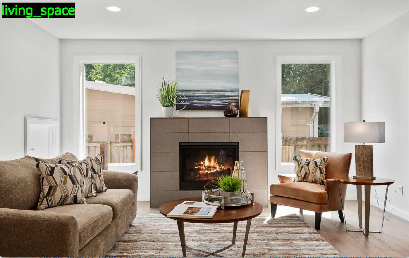 客廳設有火場、棕色沙發、椅子、咖啡桌和牆上的景觀美術。門通往戶外露台。